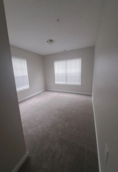 an empty room with a carpeted floor and two windows